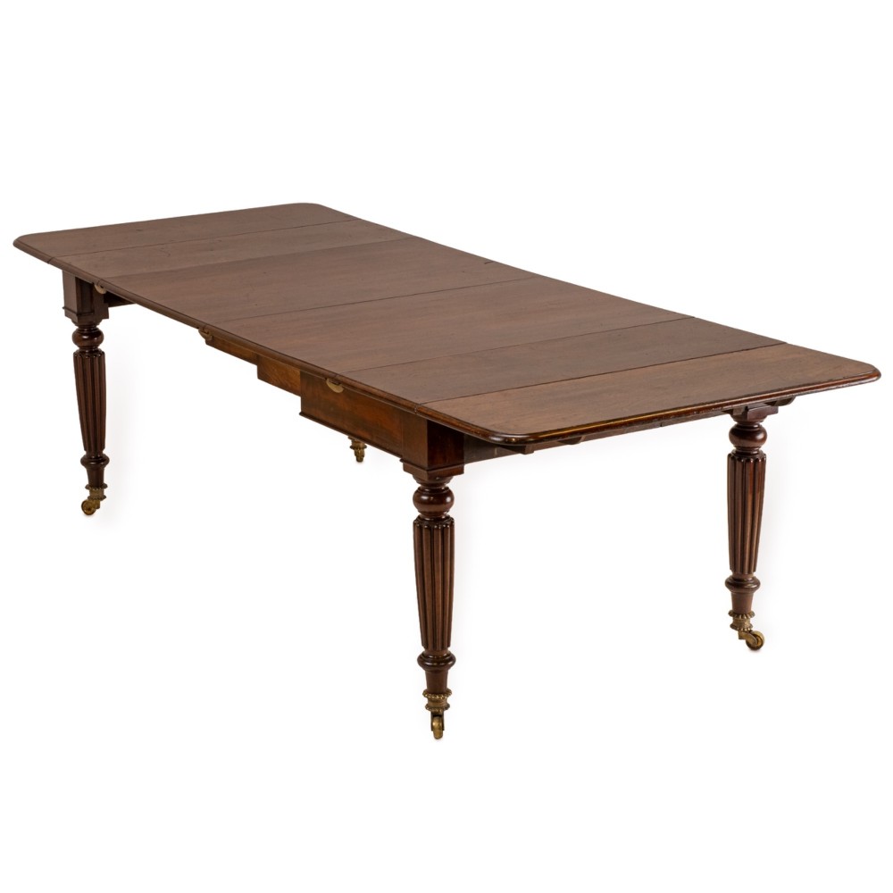 An extended Georgian mahogany dining table featuring a smooth polished surface, rectangular top with rounded corners, and reeded turned legs with brass castors.