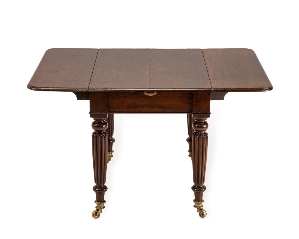An extended Georgian mahogany dining table featuring a smooth polished surface, rectangular top with rounded corners, and reeded turned legs with brass castors. View VII