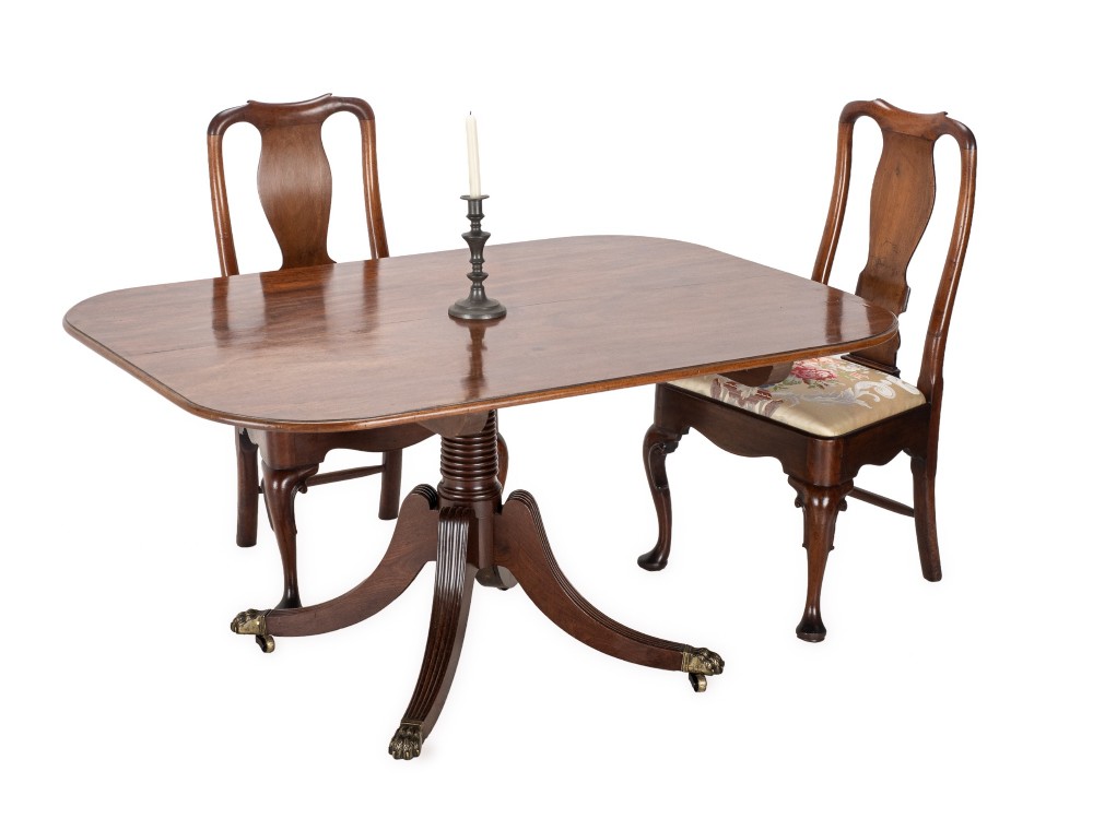 A George III mahogany dining table featuring a rectangular tilt-top surface with rounded corners set on a reeded central pedestal and four splayed legs with brass paw castors. View II