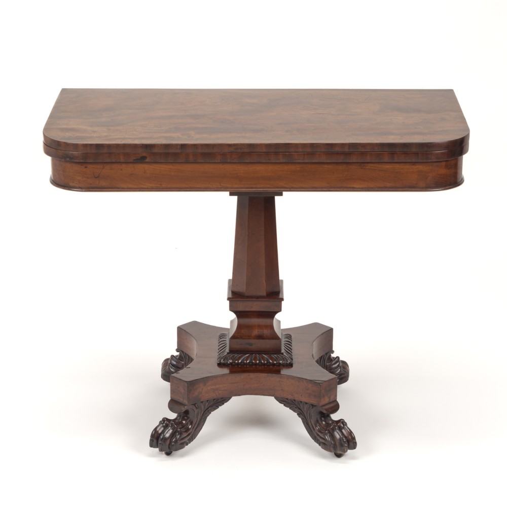 A late Regency mahogany fold-over tea table featuring a tapered central pedestal and carved paw feet on a concave quadform base.