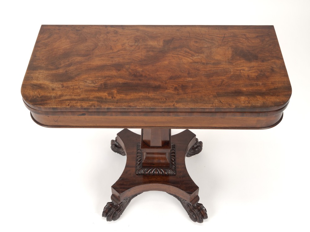 A late Regency mahogany fold-over tea table featuring a tapered central pedestal and carved paw feet on a concave quadform base. View IV