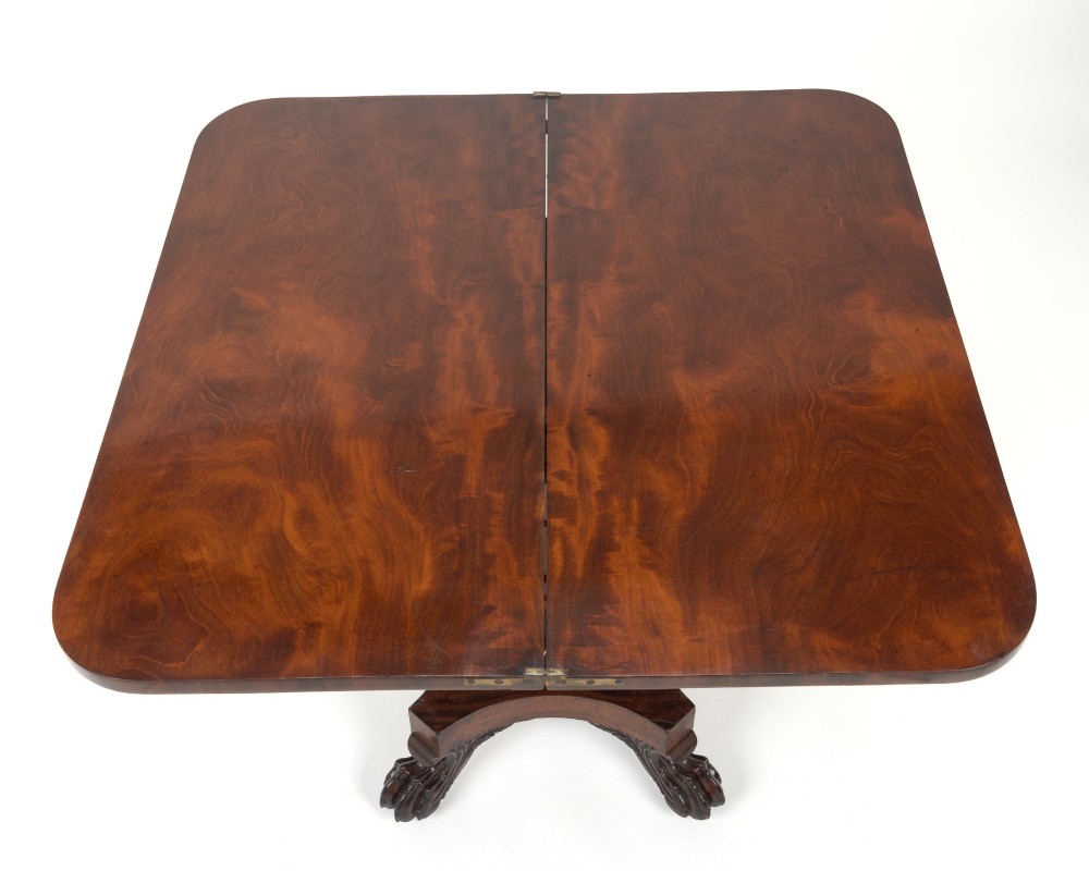 A late Regency mahogany fold-over tea table featuring a tapered central pedestal and carved paw feet on a concave quadform base. View VII