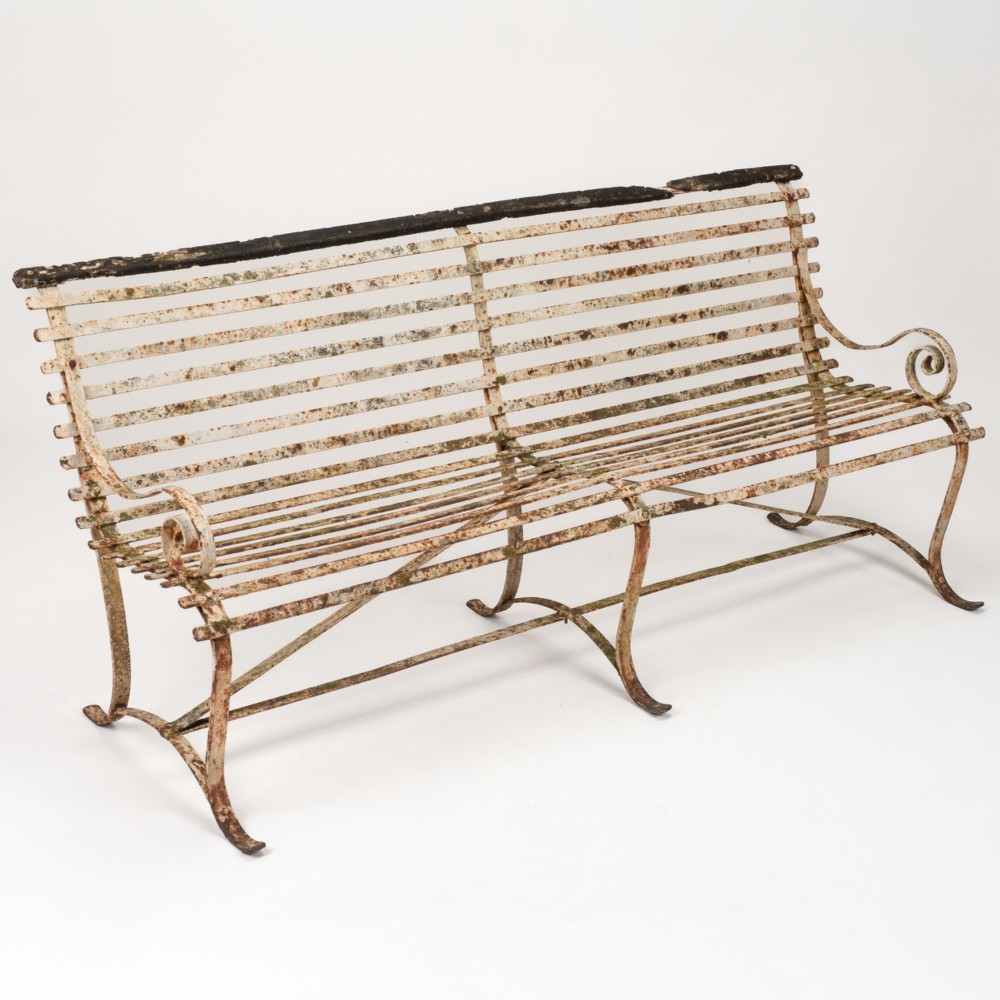 An early 19th-century Regency wrought iron garden bench featuring horizontal strapwork slats, scroll armrests, and a weathered paint finish.