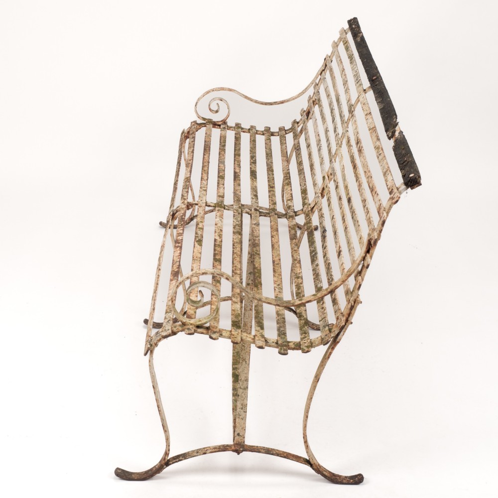An early 19th-century Regency wrought iron garden bench featuring horizontal strapwork slats, scroll armrests, and a weathered paint finish. View III