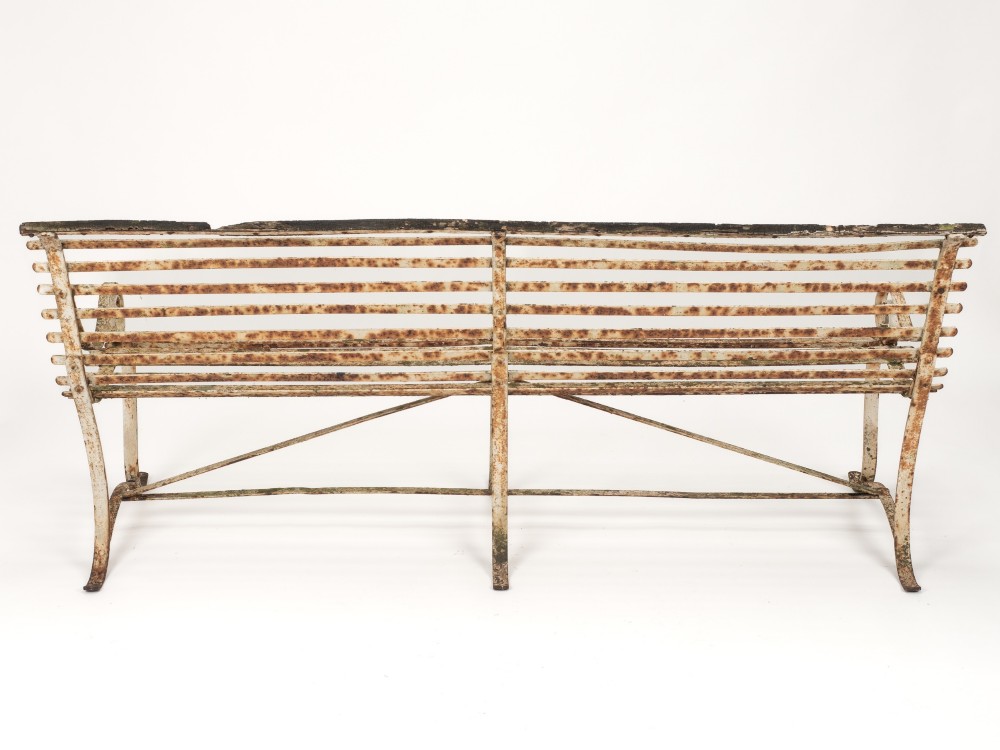 An early 19th-century Regency wrought iron garden bench featuring horizontal strapwork slats, scroll armrests, and a weathered paint finish. View IV