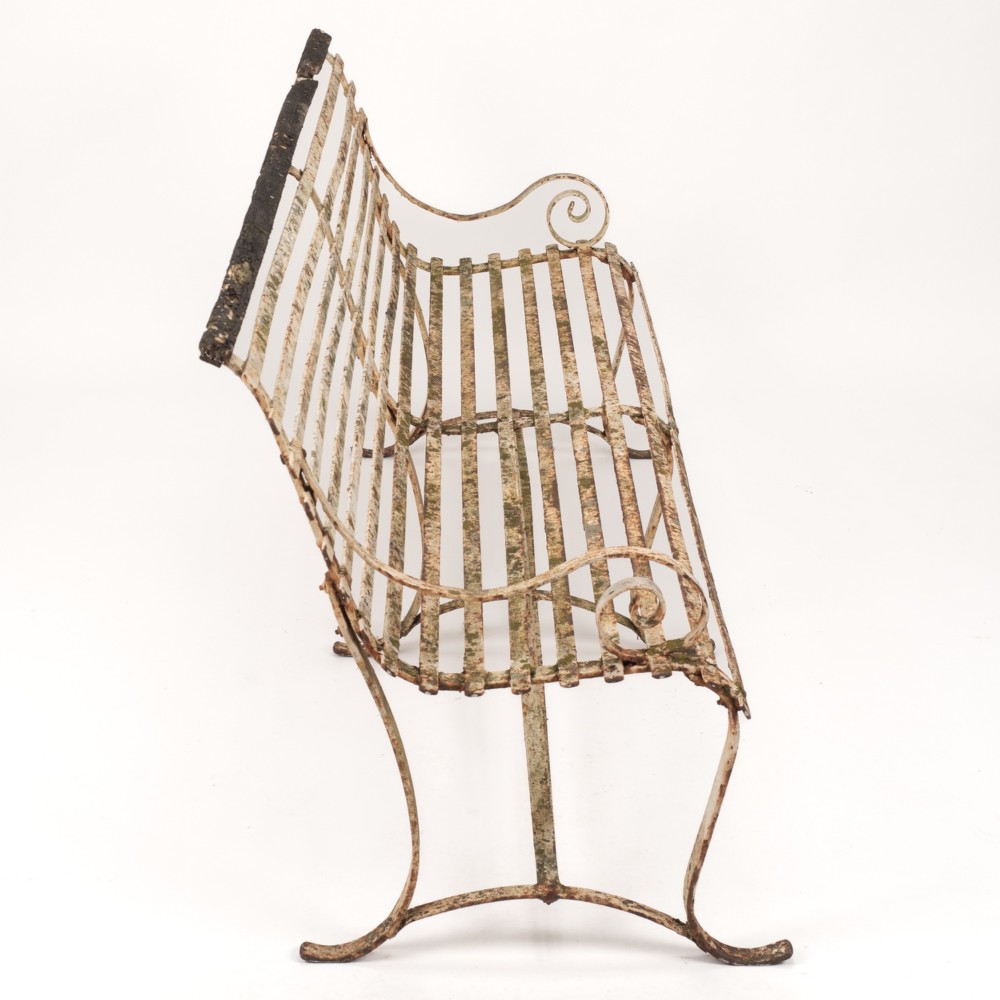 An early 19th-century Regency wrought iron garden bench featuring horizontal strapwork slats, scroll armrests, and a weathered paint finish. View V