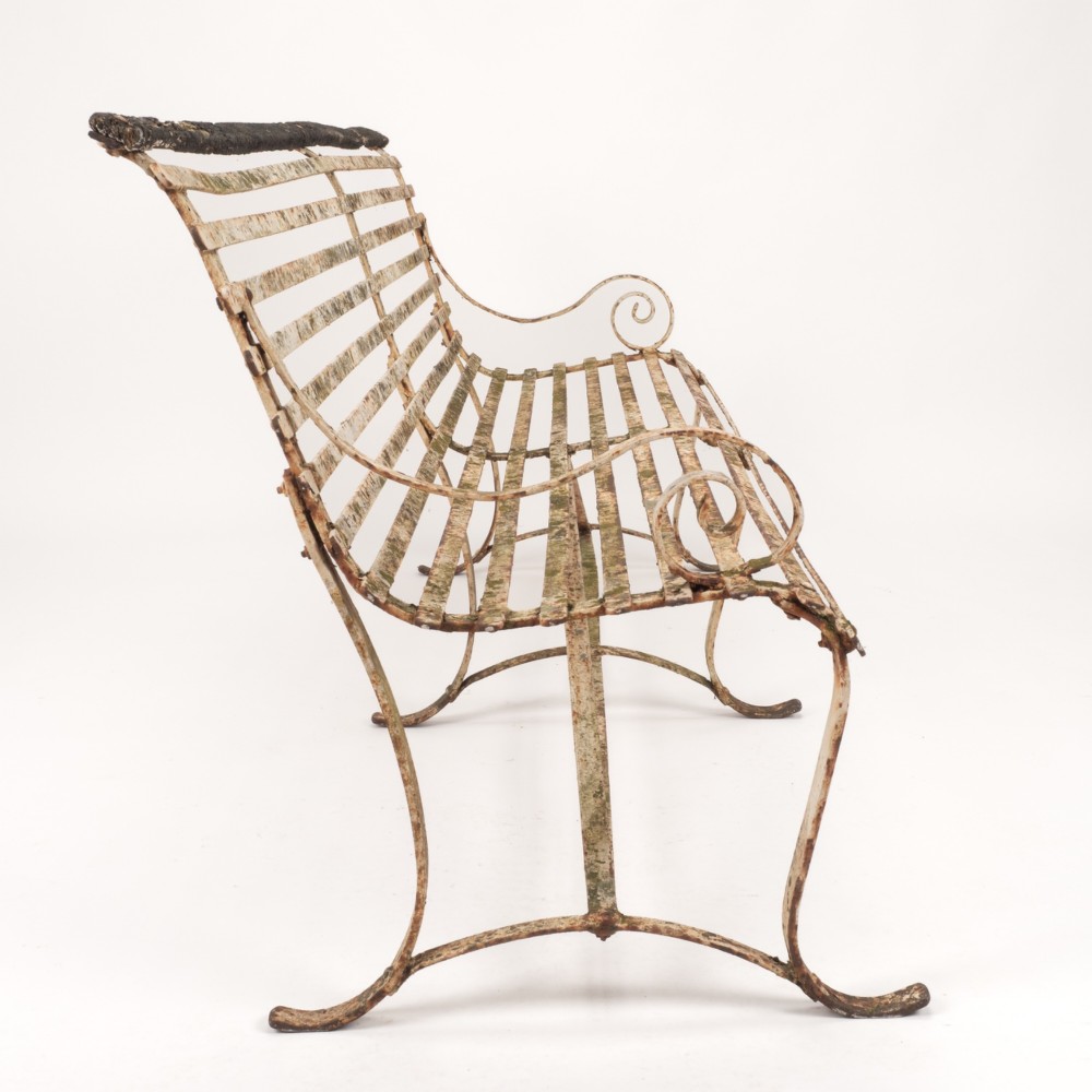An early 19th-century Regency wrought iron garden bench featuring horizontal strapwork slats, scroll armrests, and a weathered paint finish. View VI