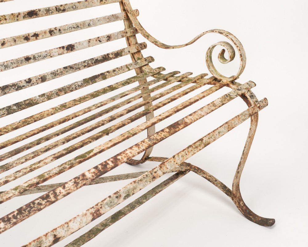 An early 19th-century Regency wrought iron garden bench featuring horizontal strapwork slats, scroll armrests, and a weathered paint finish. View VIII