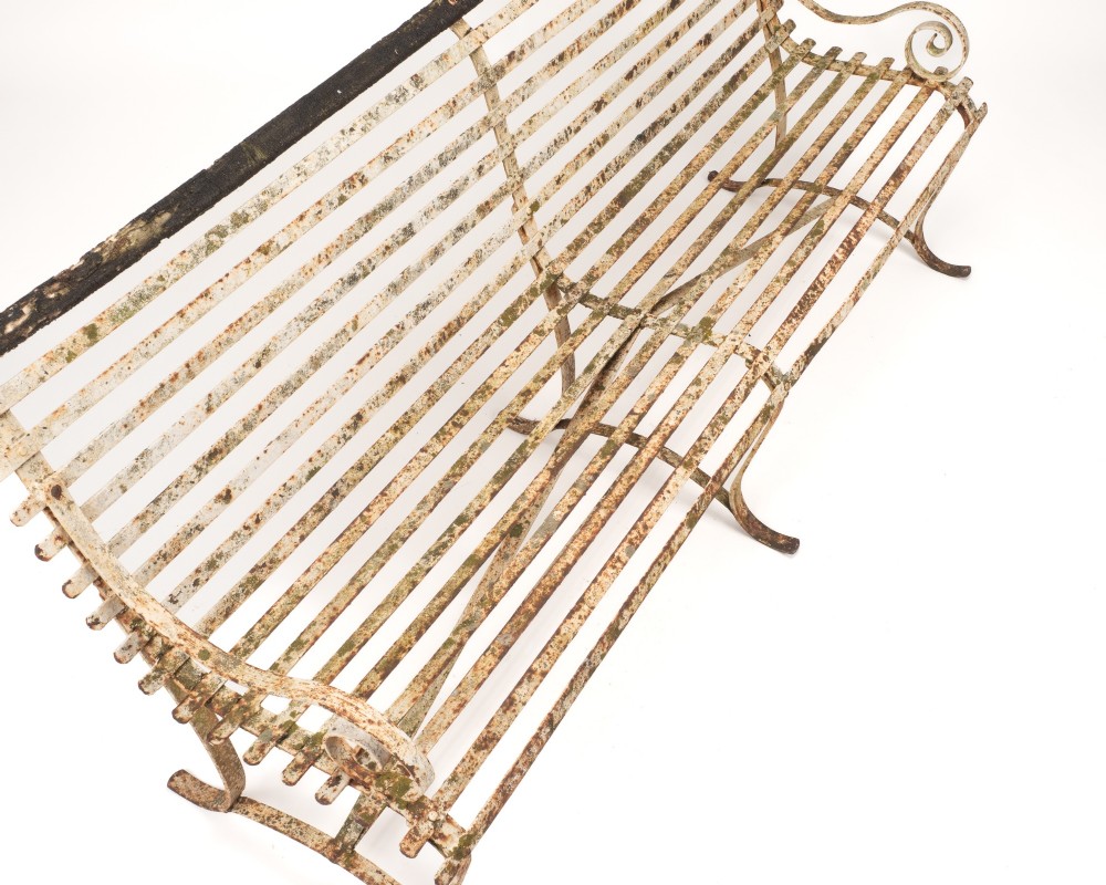 An early 19th-century Regency wrought iron garden bench featuring horizontal strapwork slats, scroll armrests, and a weathered paint finish. View X