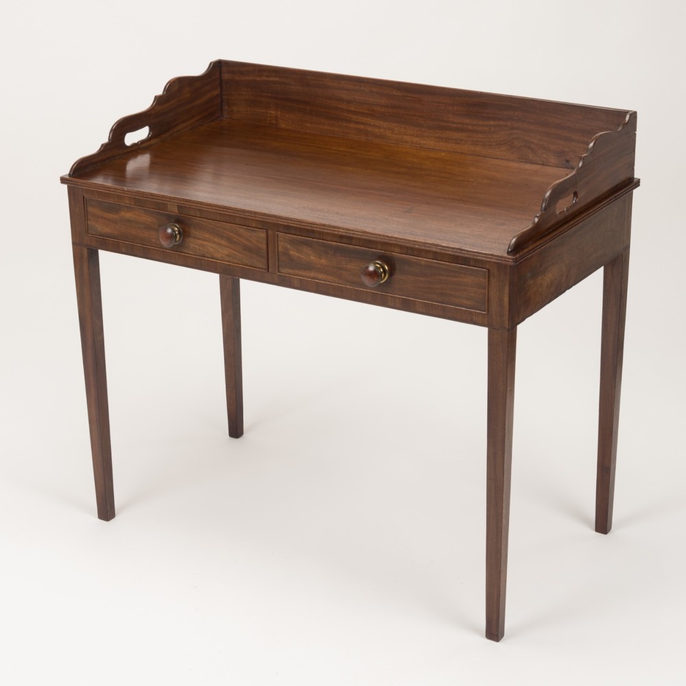 An early 19th-century mahogany tray-top writing table featuring a gallery edge with side cutout handles, two drawers with knob handles, and square tapered legs.