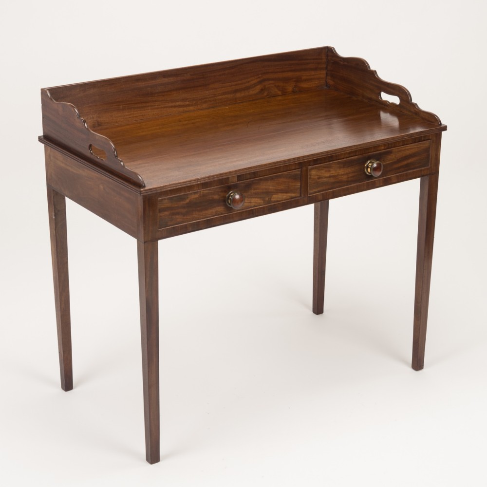 An early 19th-century mahogany tray-top writing table featuring a gallery edge with side cutout handles, two drawers with knob handles, and square tapered legs. View II
