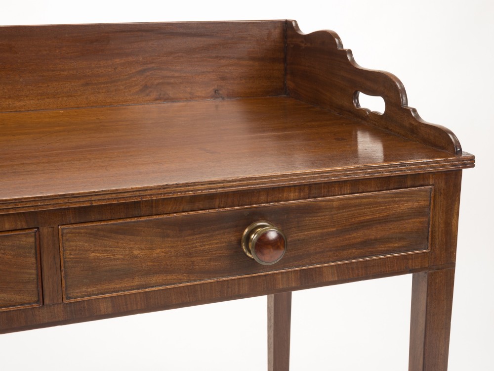 An early 19th-century mahogany tray-top writing table featuring a gallery edge with side cutout handles, two drawers with knob handles, and square tapered legs. View IV