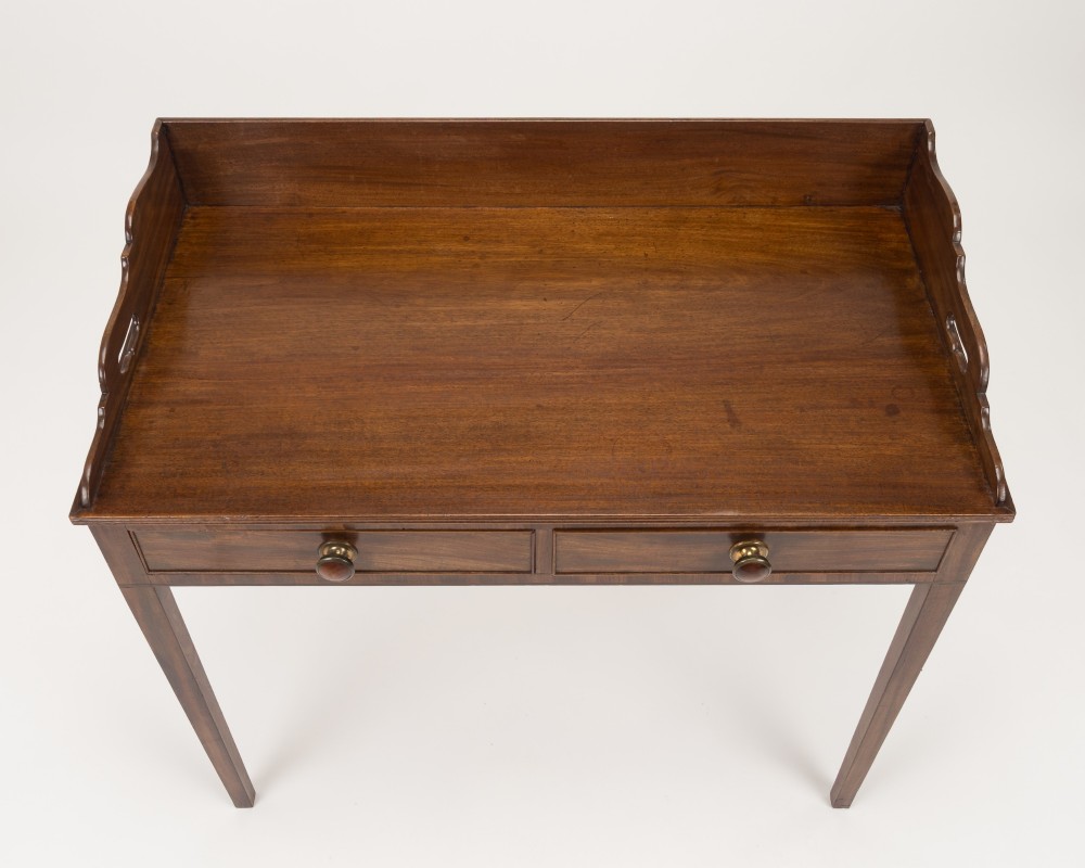 An early 19th-century mahogany tray-top writing table featuring a gallery edge with side cutout handles, two drawers with knob handles, and square tapered legs. View V
