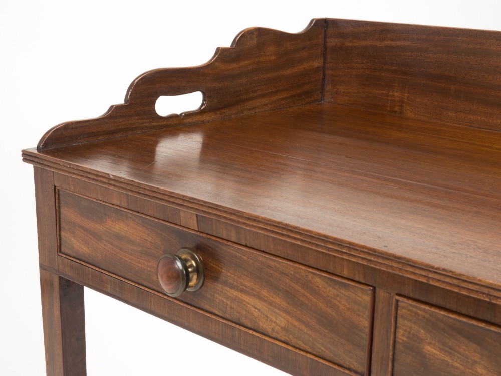 An early 19th-century mahogany tray-top writing table featuring a gallery edge with side cutout handles, two drawers with knob handles, and square tapered legs. View VI