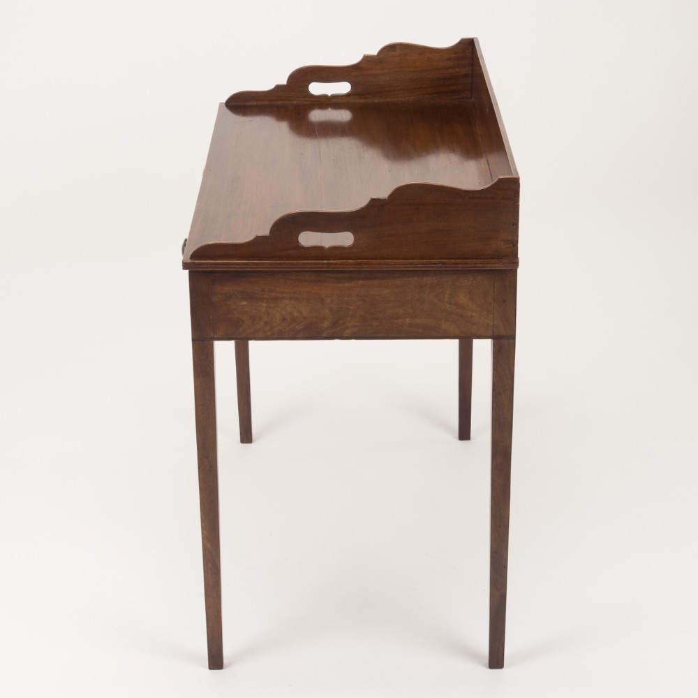 An early 19th-century mahogany tray-top writing table featuring a gallery edge with side cutout handles, two drawers with knob handles, and square tapered legs. View VII