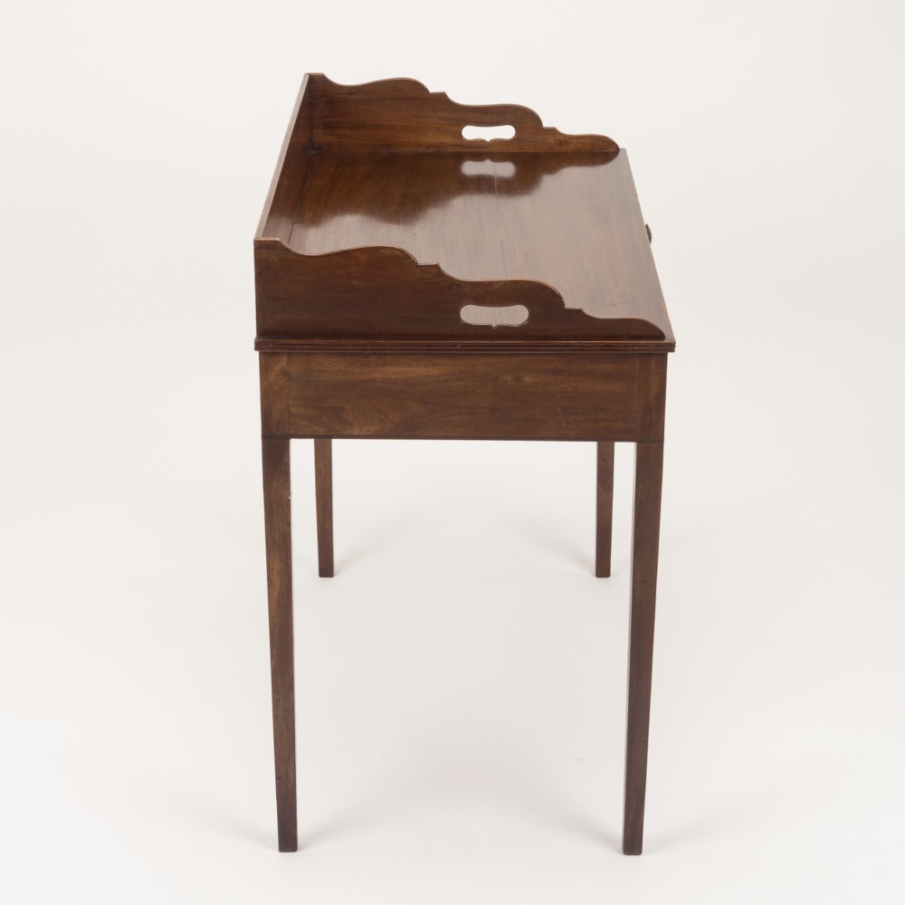 An early 19th-century mahogany tray-top writing table featuring a gallery edge with side cutout handles, two drawers with knob handles, and square tapered legs. View VIII