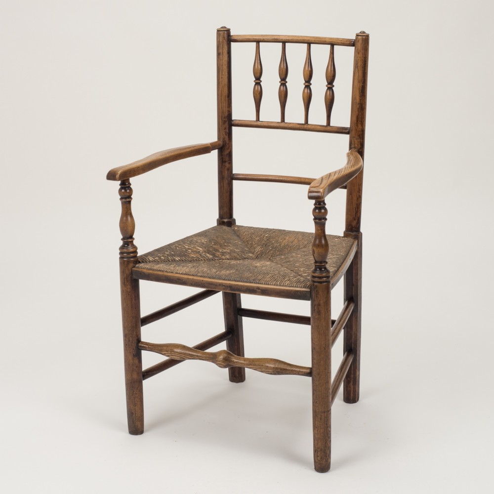 An early nineteenth-century English country armchair with a spindle back rest, curved open armrests, turned legs, and a woven rush seat.