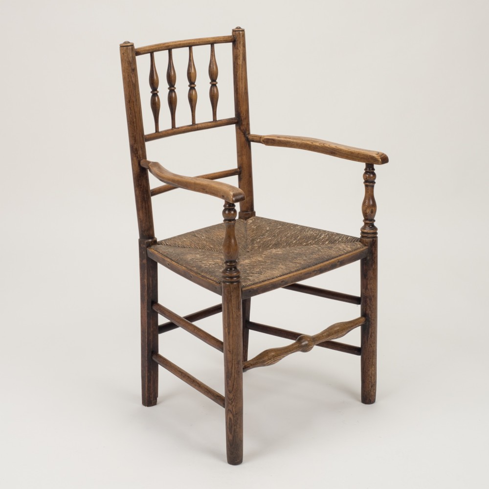 An early nineteenth-century English country armchair with a spindle back rest, curved open armrests, turned legs, and a woven rush seat. View II