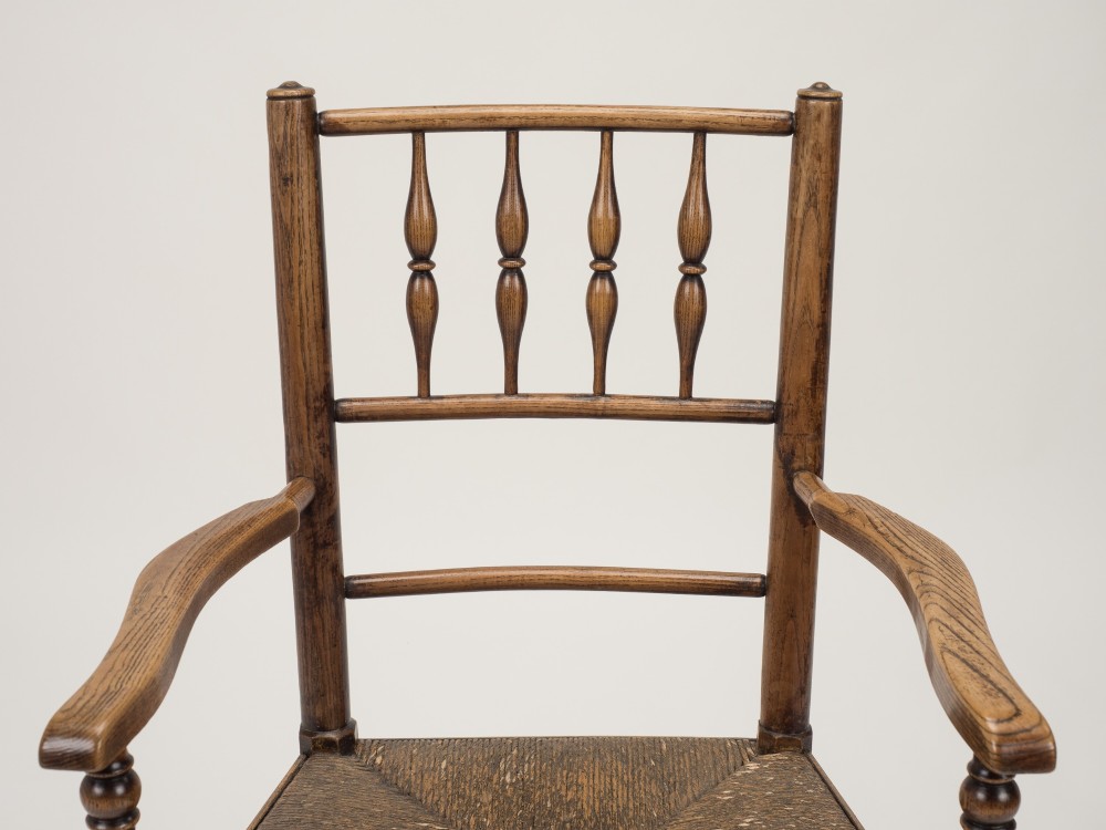 An early nineteenth-century English country armchair with a spindle back rest, curved open armrests, turned legs, and a woven rush seat. View III