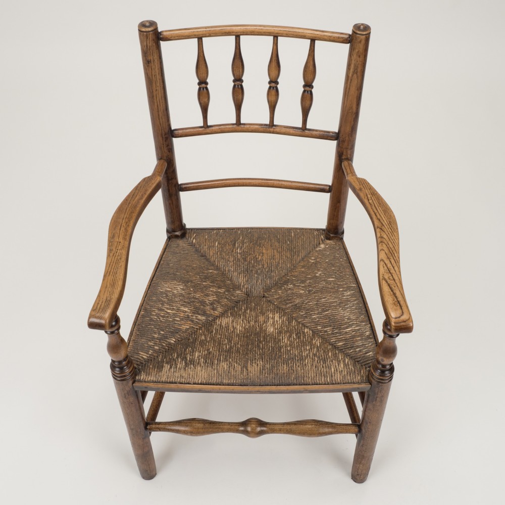 An early nineteenth-century English country armchair with a spindle back rest, curved open armrests, turned legs, and a woven rush seat. View IV