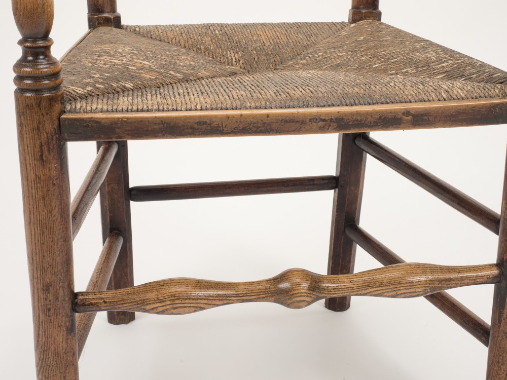 An early nineteenth-century English country armchair with a spindle back rest, curved open armrests, turned legs, and a woven rush seat. View VI