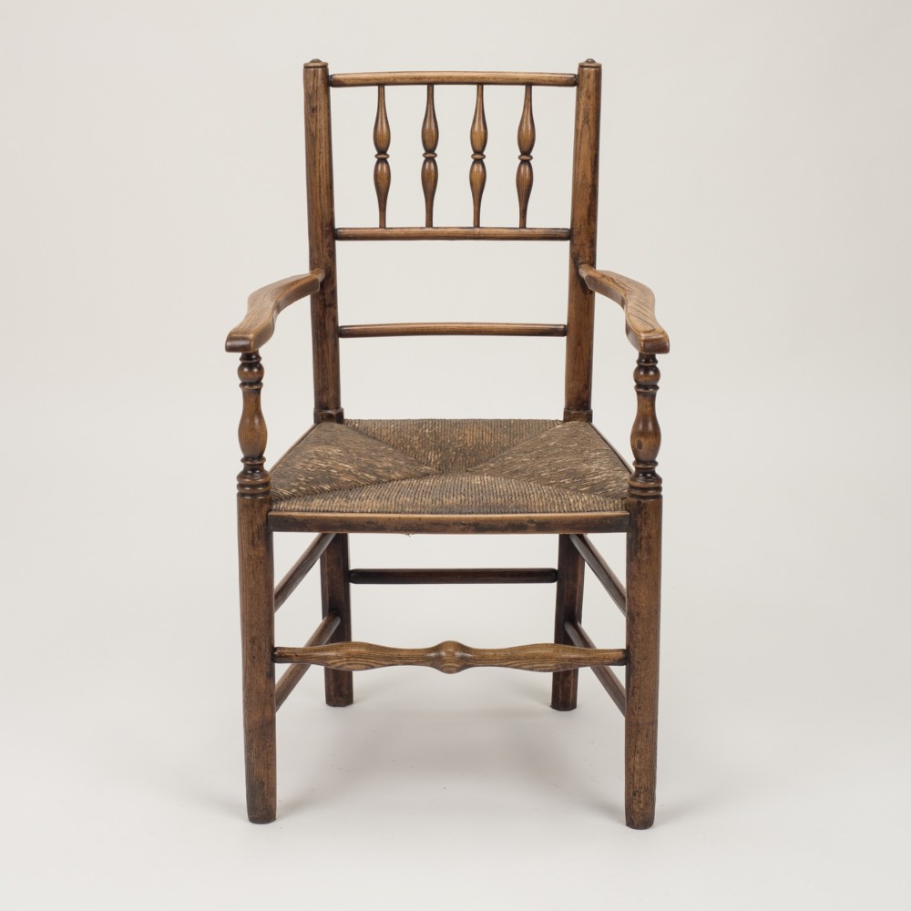An early nineteenth-century English country armchair with a spindle back rest, curved open armrests, turned legs, and a woven rush seat. View VII