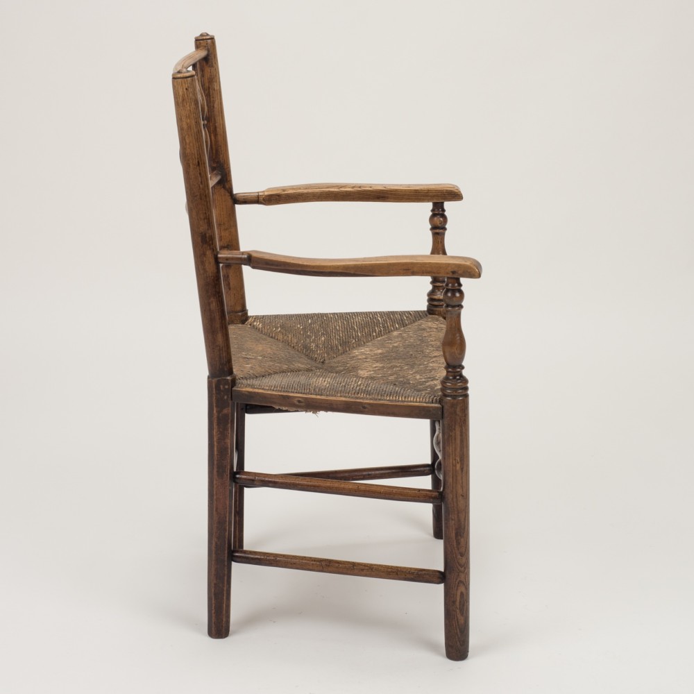 An early nineteenth-century English country armchair with a spindle back rest, curved open armrests, turned legs, and a woven rush seat. View VIII