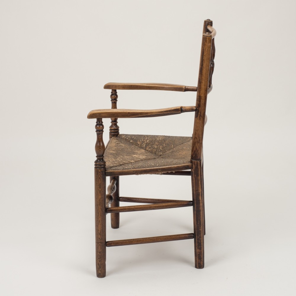 An early nineteenth-century English country armchair with a spindle back rest, curved open armrests, turned legs, and a woven rush seat. View IX