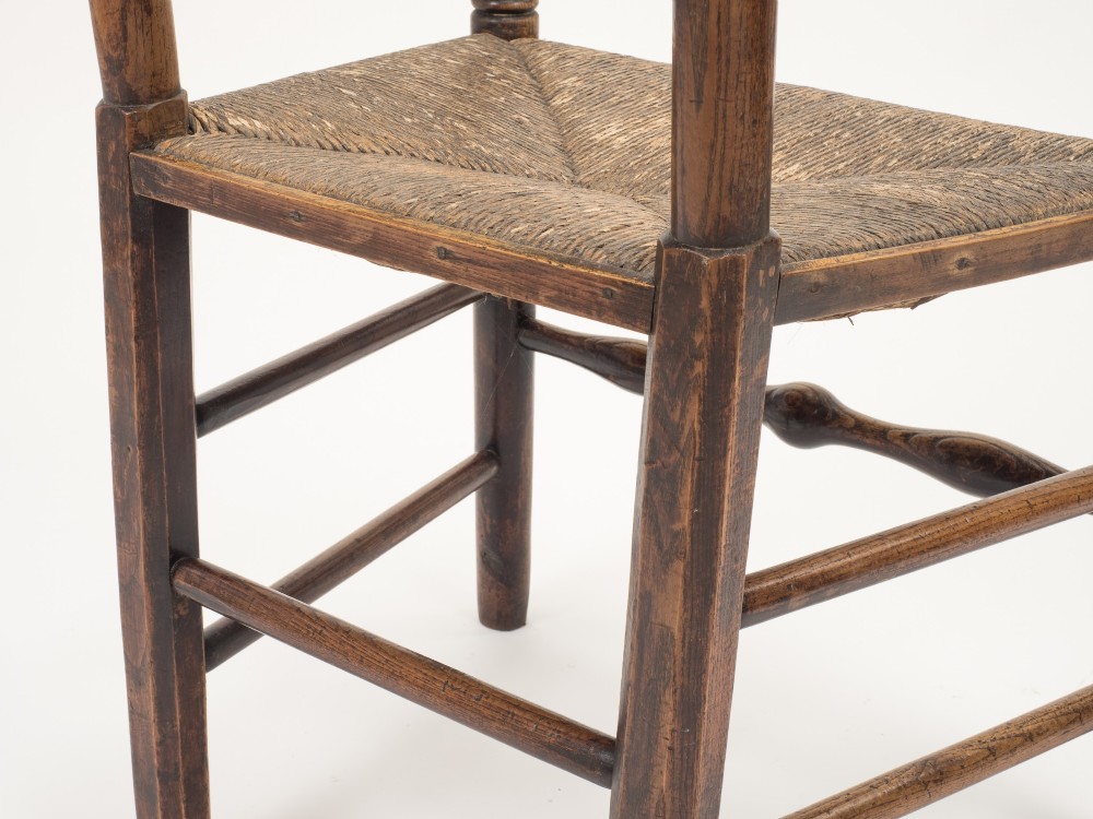 An early nineteenth-century English country armchair with a spindle back rest, curved open armrests, turned legs, and a woven rush seat. View XI