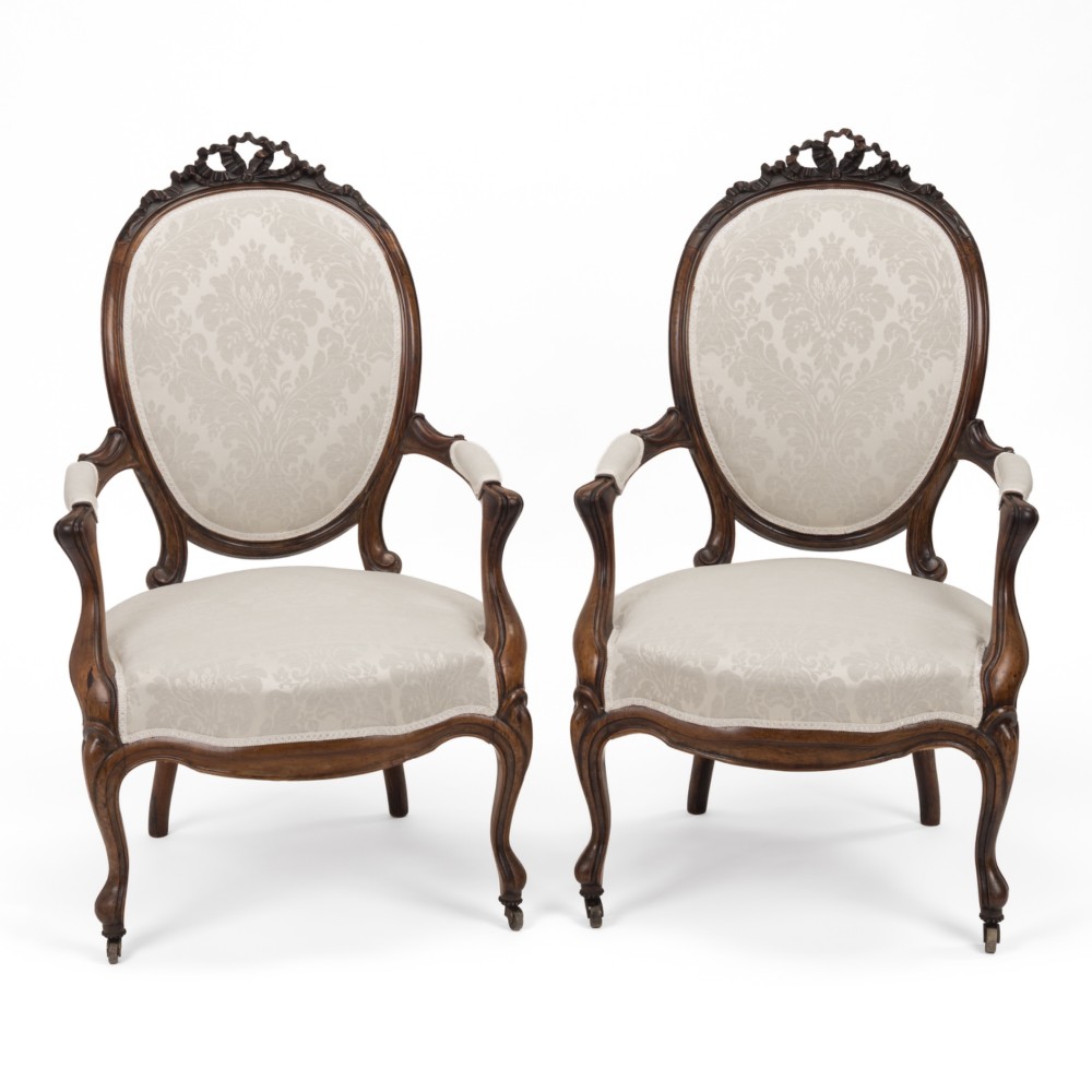 A pair of mid-19th century English rosewood Rococo Revival open armchairs with oval damask backs, carved top crests, padded arms, and cabriole legs on castors.