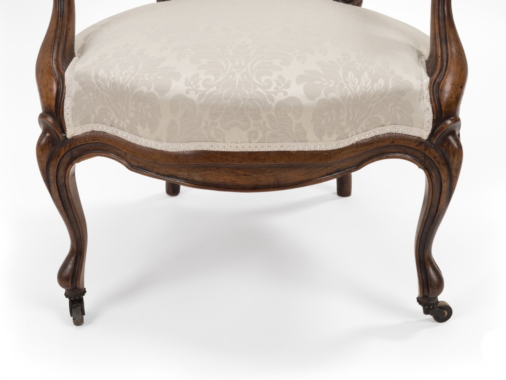 A pair of mid-19th century English rosewood Rococo Revival open armchairs with oval damask backs, carved top crests, padded arms, and cabriole legs on castors. View V