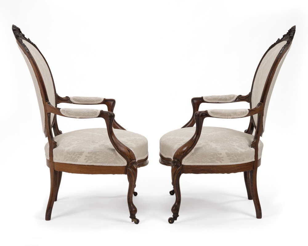 A pair of mid-19th century English rosewood Rococo Revival open armchairs with oval damask backs, carved top crests, padded arms, and cabriole legs on castors. View X