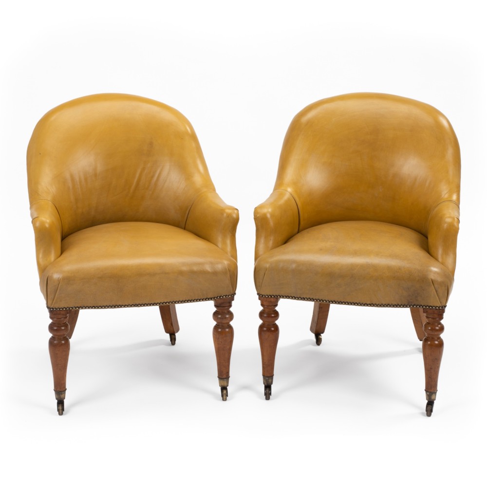 A pair of early 19th-century Regency library armchairs upholstered in warm tan leather with turned maple front legs on brass castors.