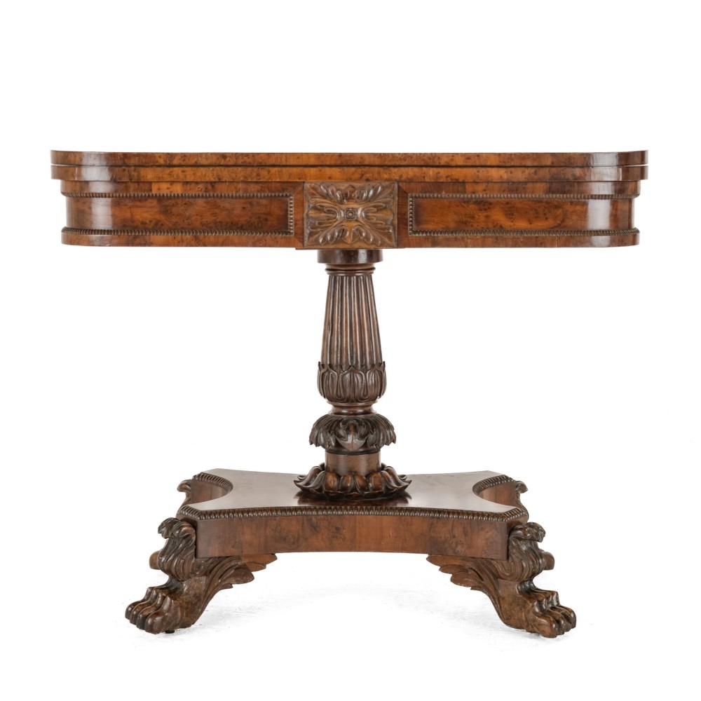 A William IV burr yew wood card table with a rectangular fold-over swivel top, carved apron detail, fluted pedestal column, and a shaped plinth base on carved claw feet.