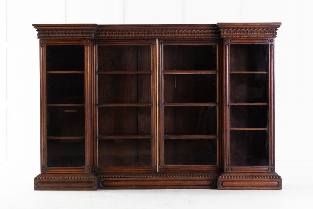 A nineteenth-century Anglo-Indian breakfront bookcase made of dark padouk wood with four glazed doors and carved upper mouldings.