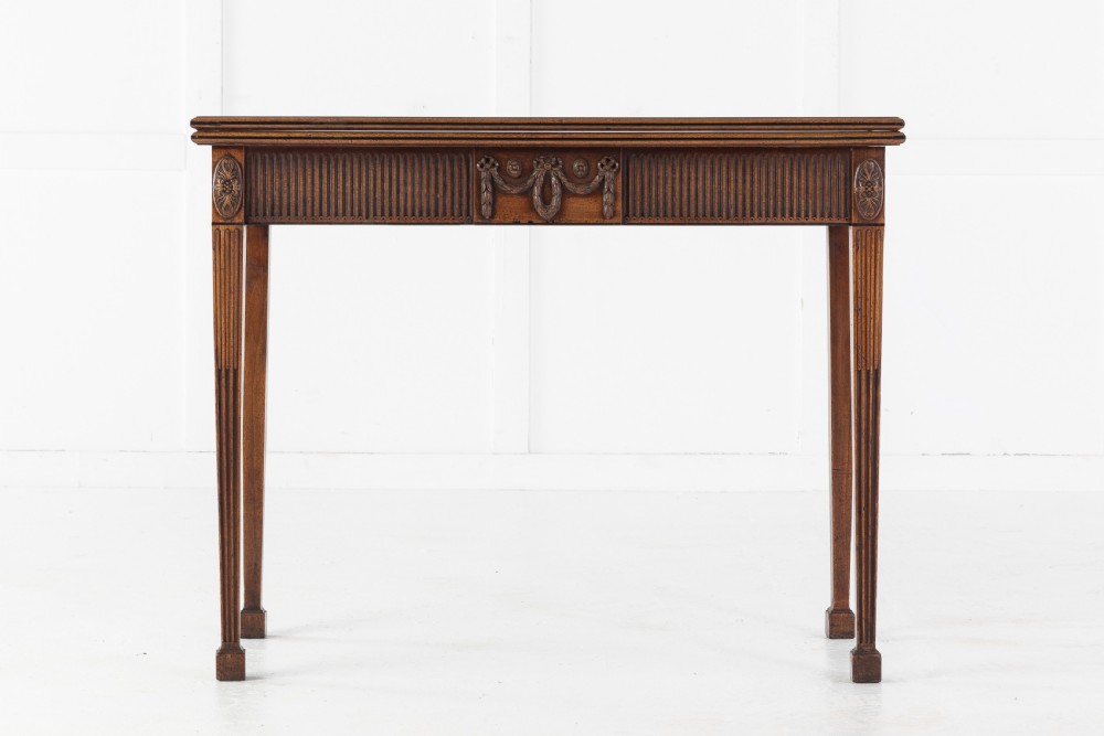 An 18th-century George III mahogany tea table featuring fluted tapering square legs, a reeded frieze with central carved floral swags, and a fold-over top. View II