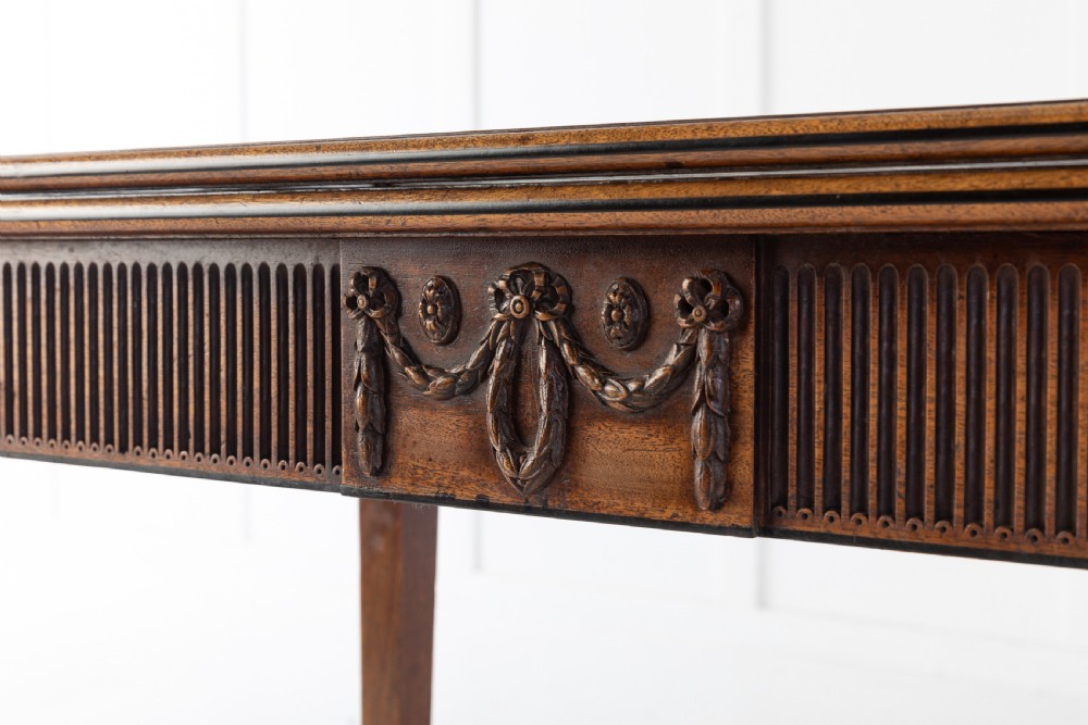 An 18th-century George III mahogany tea table featuring fluted tapering square legs, a reeded frieze with central carved floral swags, and a fold-over top. View IV
