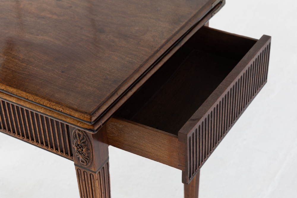An 18th-century George III mahogany tea table featuring fluted tapering square legs, a reeded frieze with central carved floral swags, and a fold-over top. View VI