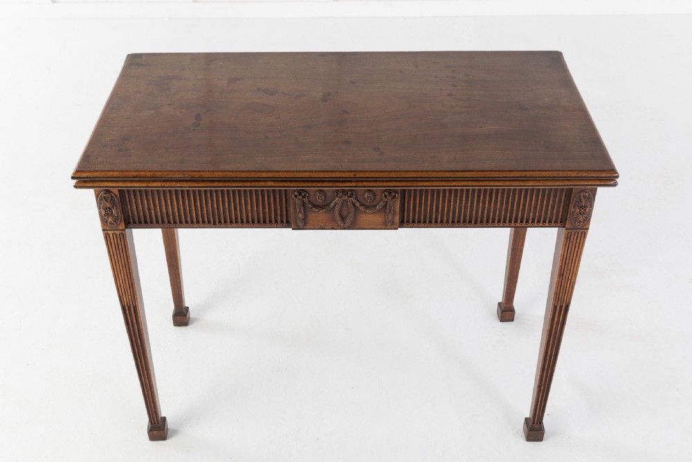 An 18th-century George III mahogany tea table featuring fluted tapering square legs, a reeded frieze with central carved floral swags, and a fold-over top. View VII