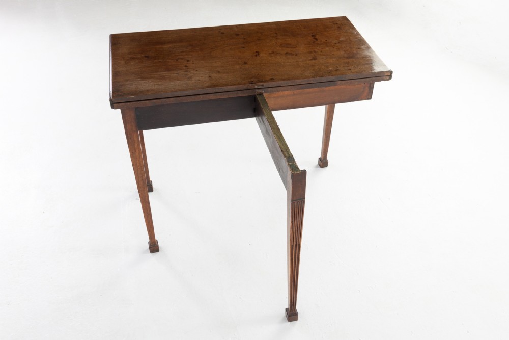 An 18th-century George III mahogany tea table featuring fluted tapering square legs, a reeded frieze with central carved floral swags, and a fold-over top. View IX