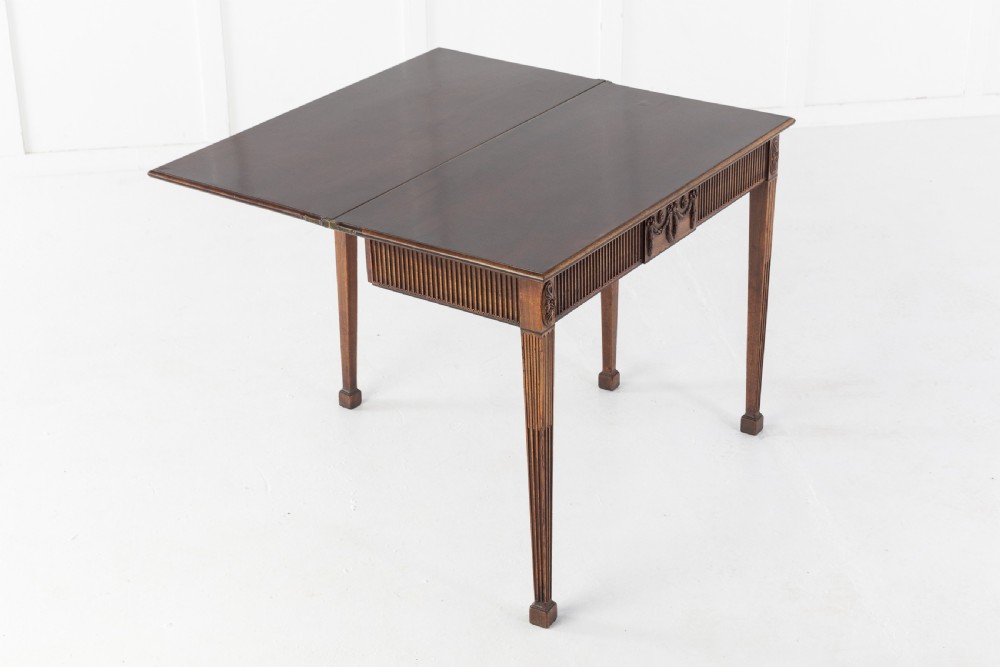 An 18th-century George III mahogany tea table featuring fluted tapering square legs, a reeded frieze with central carved floral swags, and a fold-over top. View X