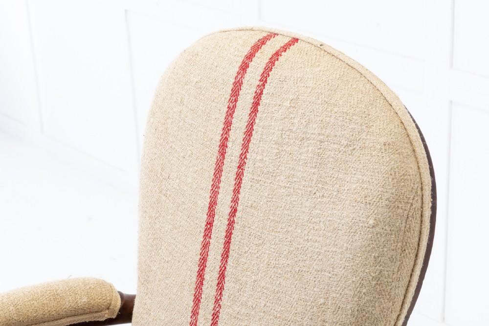A 19th-century mahogany armchair featuring turned legs on brass castors, a contoured wooden saddle seat, padded armrests, and a beige linen upholstered backrest with central red stripes. View VI