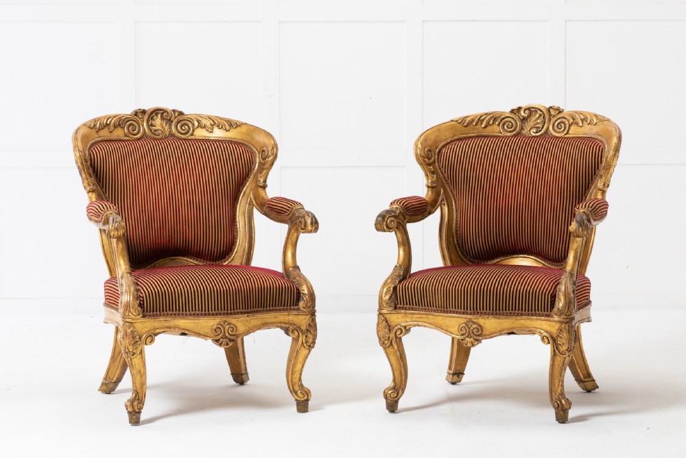A pair of 18th-century Italian giltwood armchairs with carved scroll motifs and red and gold striped fabric upholstery.