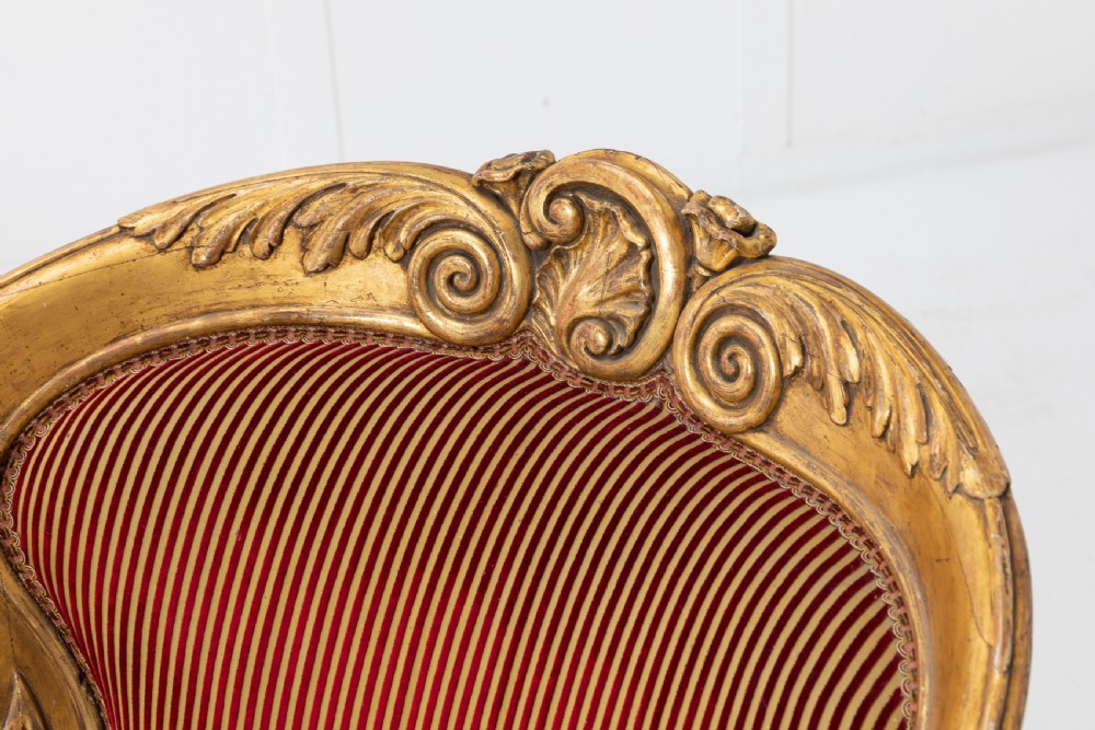 A pair of 18th-century Italian giltwood armchairs with carved scroll motifs and red and gold striped fabric upholstery. View V