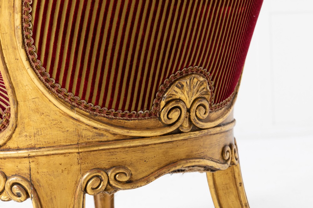 A pair of 18th-century Italian giltwood armchairs with carved scroll motifs and red and gold striped fabric upholstery. View IX