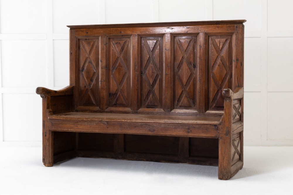 An 18th-century Spanish pine high-backed settle bench featuring carved diamond panels and curved armrests.