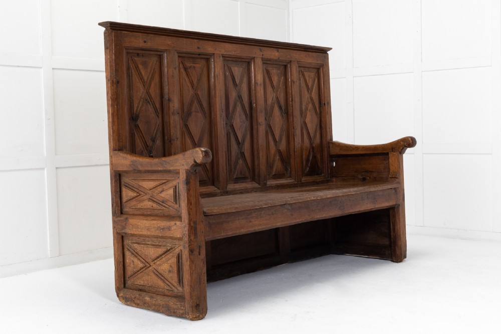 An 18th-century Spanish pine high-backed settle bench featuring carved diamond panels and curved armrests. View IV