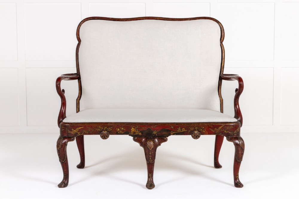 A 1930s English red Japanned settee with Chinoiserie decoration, cabriole legs, and light neutral upholstery.