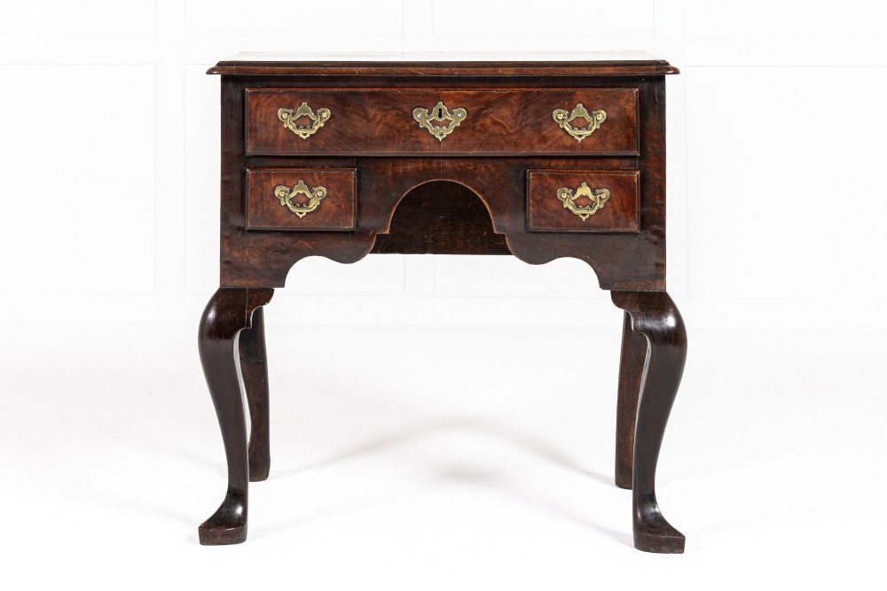 A George II mahogany lowboy featuring three drawers, brass backplate handles, a shaped apron, and four cabriole legs with pad feet.