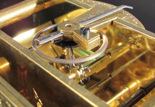 fig 2. An engraved gilt brass antique French carriage clock featuring glass side panels, an overhead folding handle, and a white enamel dial with blue Roman numerals.